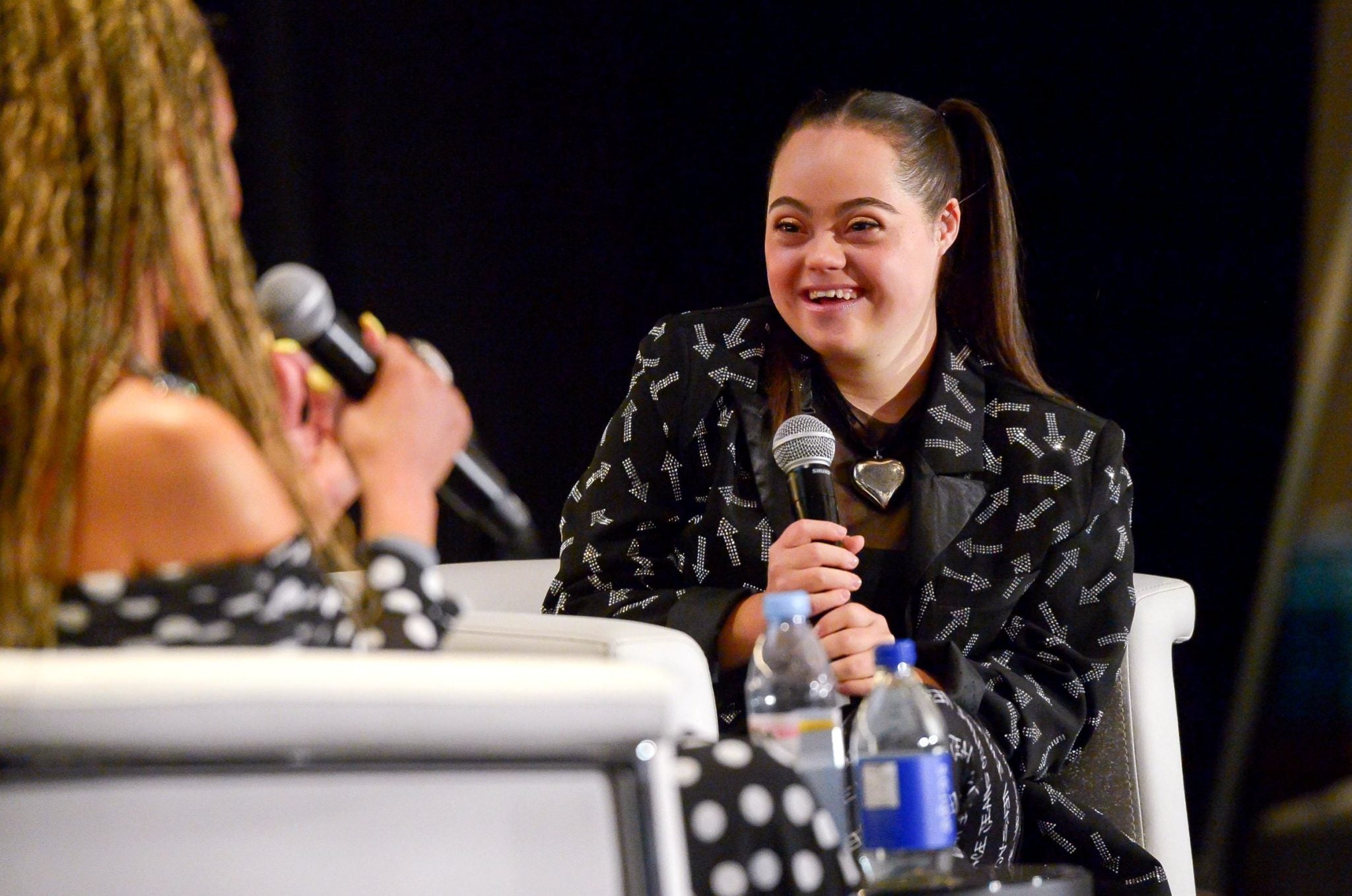 Madison speaking on stage with a microphone, smiling during an event.