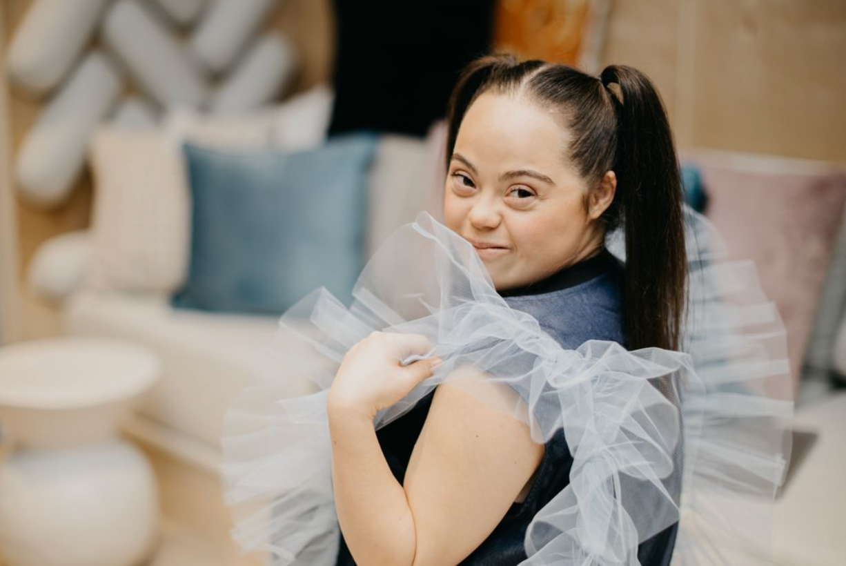 Madison smiling warmly, wearing a black top with tulle details, looking directly at the camera.